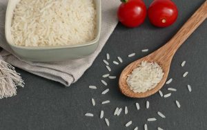 Un piatto di riso bianco accanto a dei pomodori e un cucchiaio su un tavolo